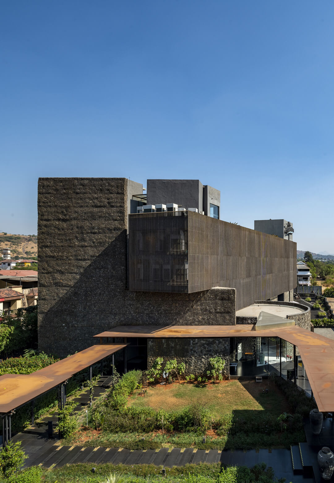 Radisson Lonavala by Malik Architecture seamlessly integrates raw concrete forms and stone-clad facades into the lush natural landscape, creating a monolithic yet organic presence | Radisson Lonavala