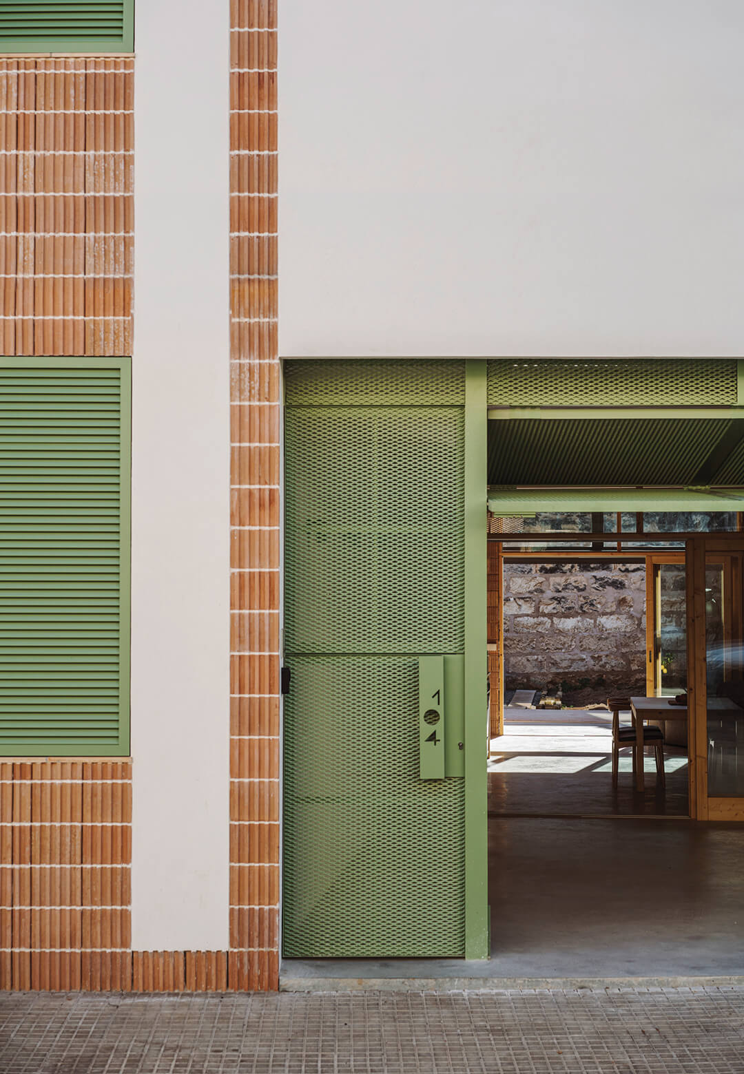 En Bateria is a singly family home on a plot with party walls;  a green metal mesh door allows ventilation and provides a contrast to the home’s muted tones | En Bateria | NORA Studio | STIRworld