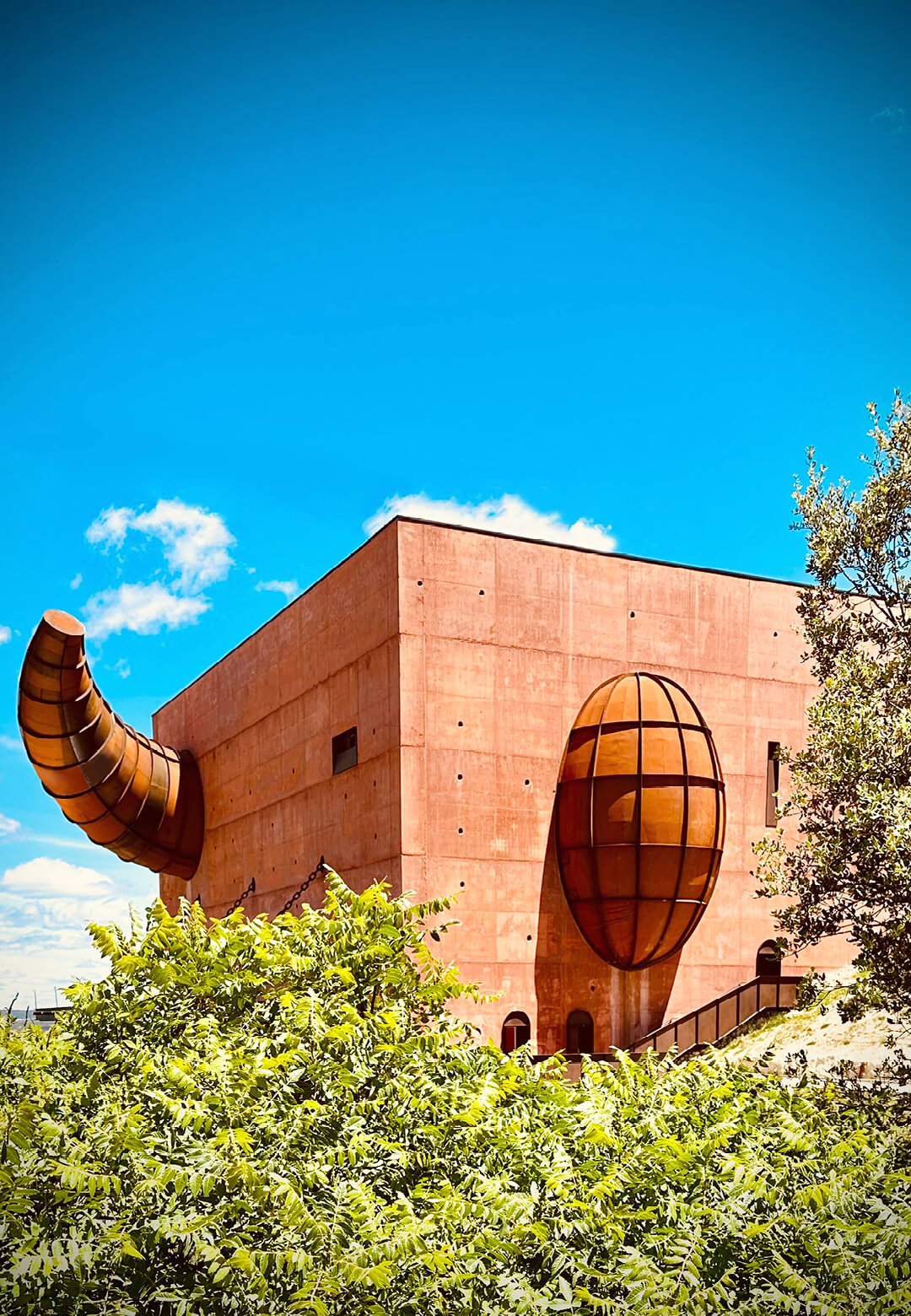The striking terracotta facade amidst lush olive groves, blends harmoniously with the rugged Spanish landscape, while its sculptural detail exudes a sense of mystery  | LA Almazara | Philippe Starck |